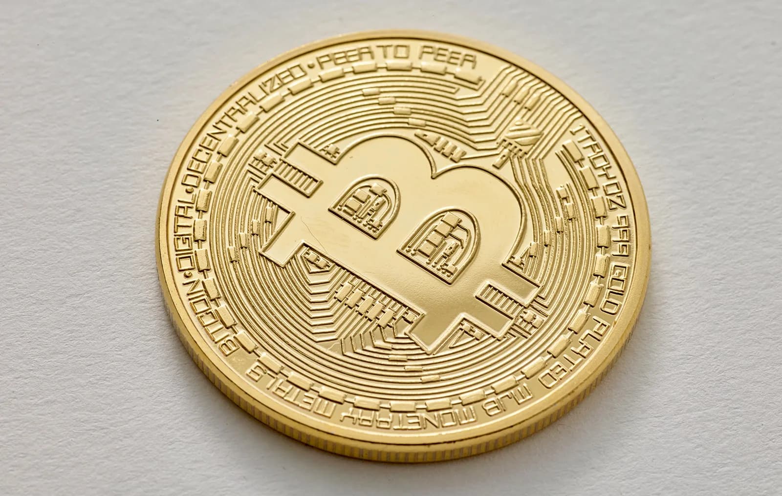 Gold Bitcoin token embossed with the B symbol on a pale surface